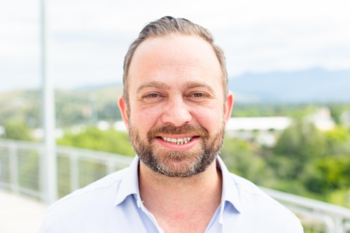 Headshot of Garrett Cathcart, a white man with a salt and pepper beard standing in front of scenic mountains