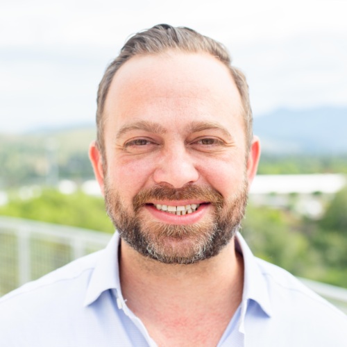 Headshot of Garrett Cathcart, a white man with a salt and pepper beard standing in front of scenic mountains