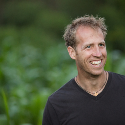 Jake Harriman, a tall white man with blonde hair, smiling in front of a grassy field