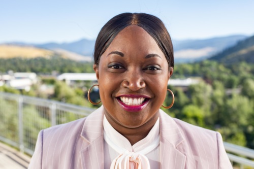 headshot of Mary Tobin, a Black woman, wearing a light pink jacket and white blouse, with mountains in the background