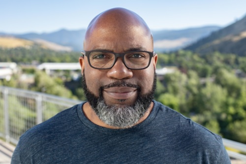 headshot of Jarrad Turner, a bald Black man with glasses and beard, with mountains in the background