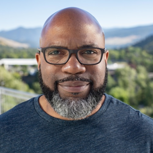 headshot of Jarrad Turner, a bald Black man with glasses and beard, with mountains in the background