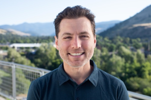 headshot of Ben Bain, white man in blue collared shirt, with mountains in the background