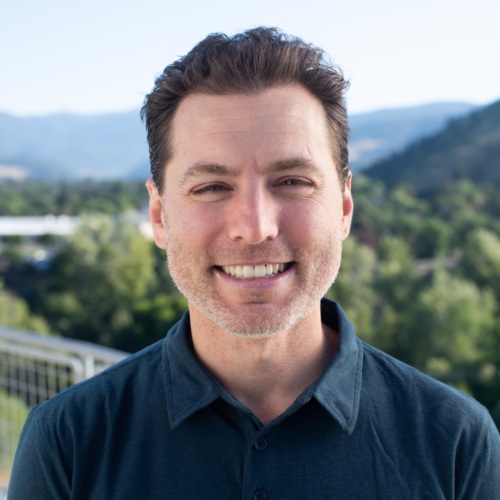 headshot of Ben Bain, white man in blue collared shirt, with mountains in the background