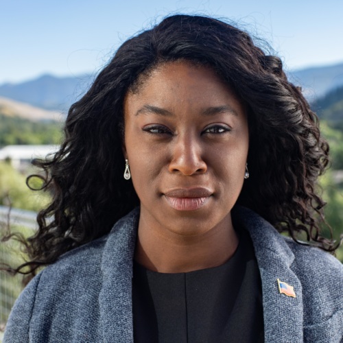 headshot of Charlynda Scales, a Black woman wearing a blue blazer, and mountains in the background