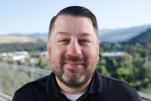 headshot of Ric Chavez, a Hispanic man wearing a collared shirt, with mountains in the background