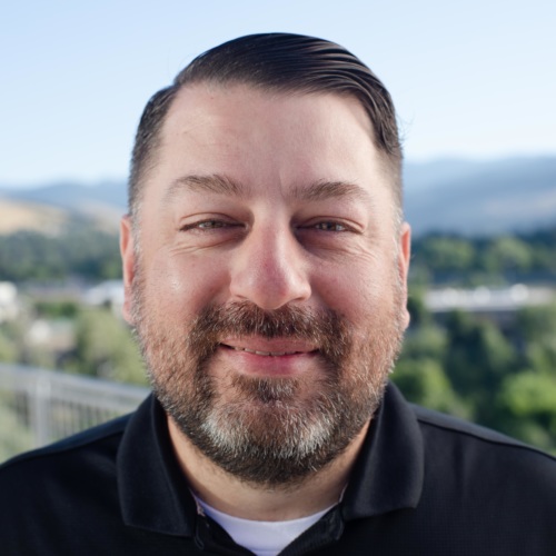 headshot of Ric Chavez, a Hispanic man wearing a collared shirt, with mountains in the background