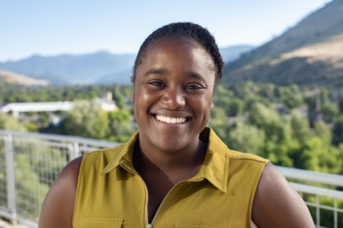Headshot of Sidney Covington, a Black woman wearing a green collared shirt, and mountains in the background.