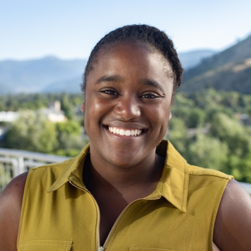 Headshot of Sidney Covington, a Black woman wearing a green collared shirt, and mountains in the background.