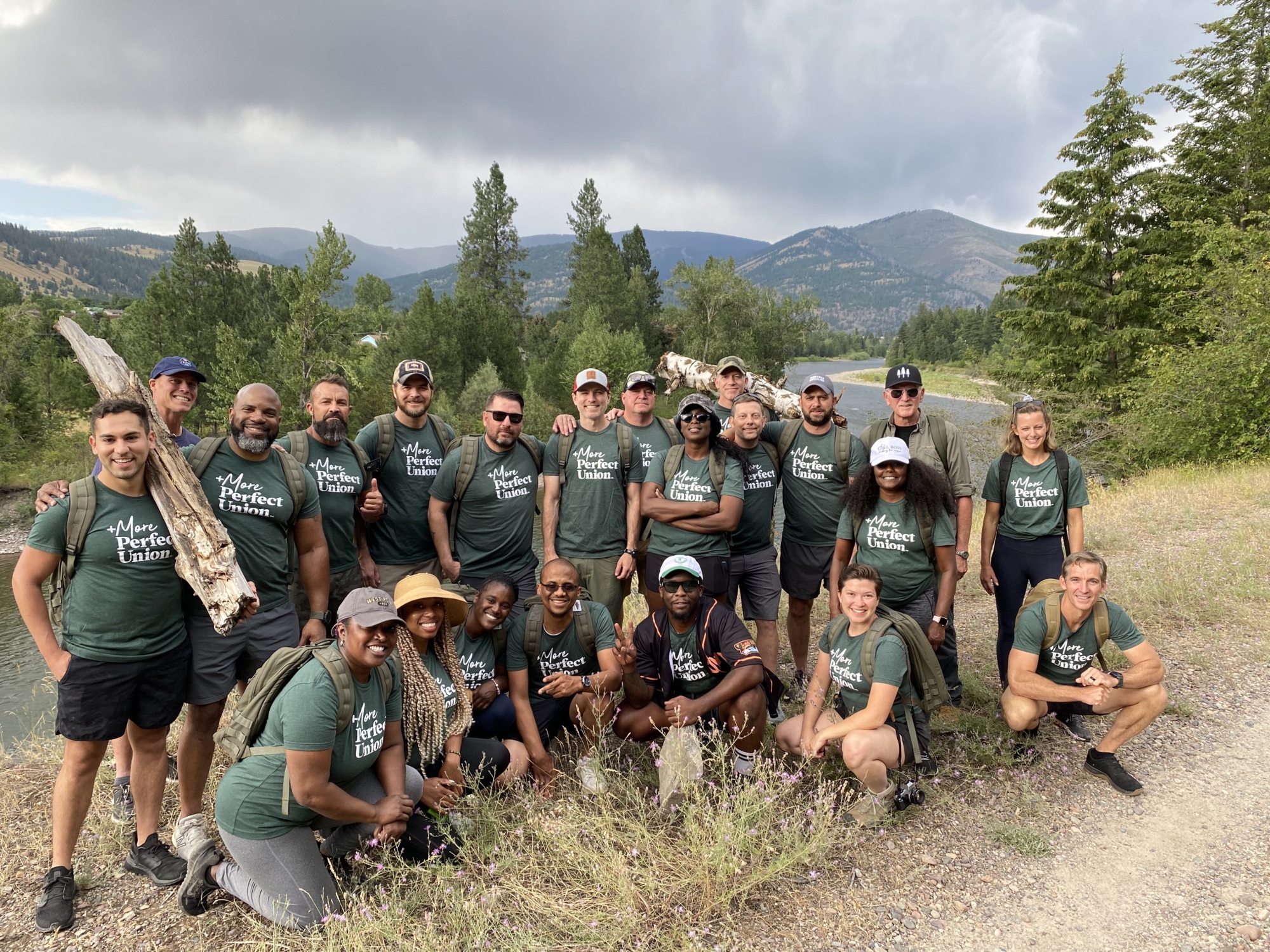 a group of people who are Black, white, and Hispanic wearing green shirts that say More Perfect Union while on a hike in Montana.