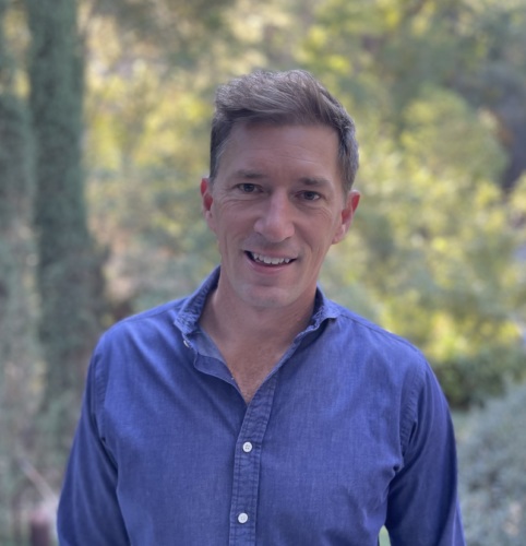 Headshot of Jason Mayo, a white male with a blue button up shirt with trees in the background