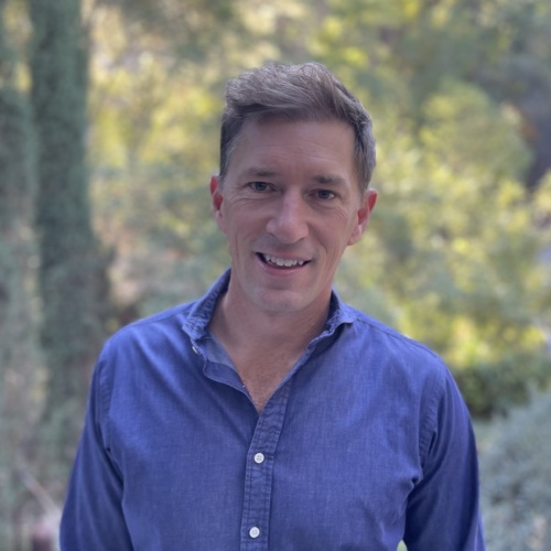 Headshot of Jason Mayo, a white male with a blue button up shirt with trees in the background