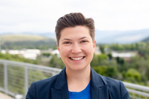 Headshot of Victoria Rametta, a nonbinary femme with short brown hair standing in front of scenic mountains