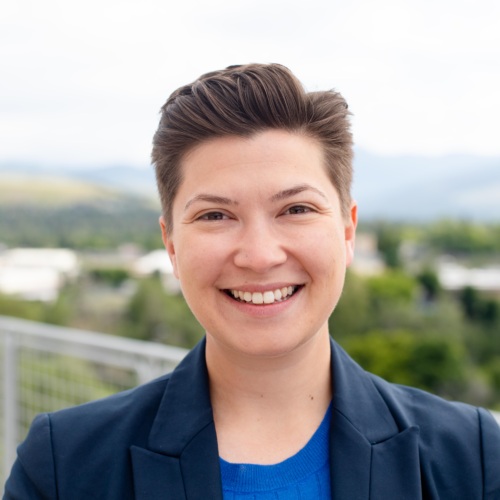 Headshot of Victoria Rametta, a nonbinary femme with short brown hair standing in front of scenic mountains