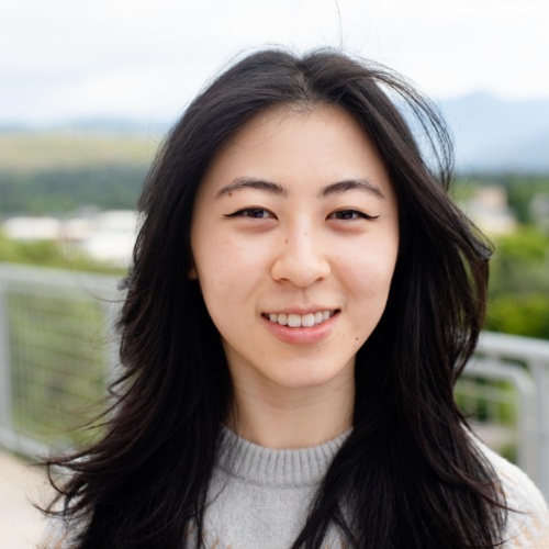 headshot of Maina Chen, an Asian woman with long dark hair in a grey and beige sweater with mountains in the background.