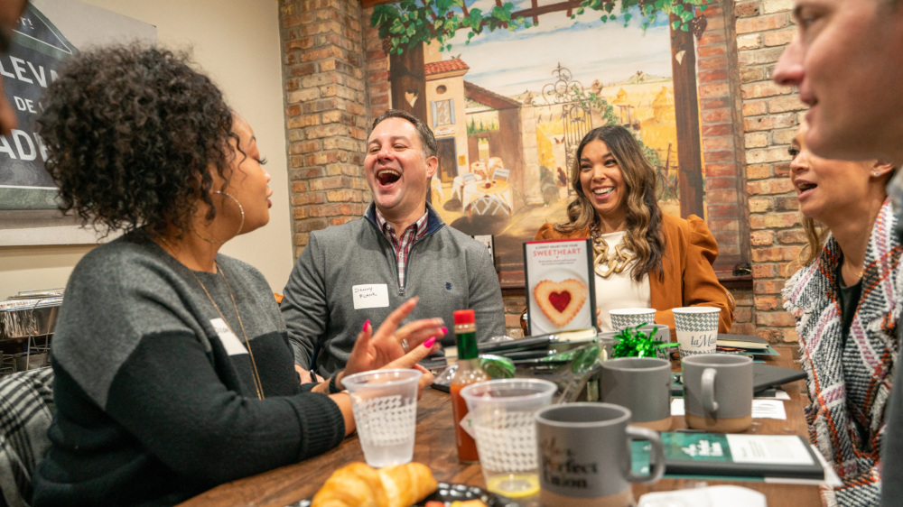 Close up photo of 5 people ranging from Black, white, hispanic, and Asian races at an MPU brunch laughing together.