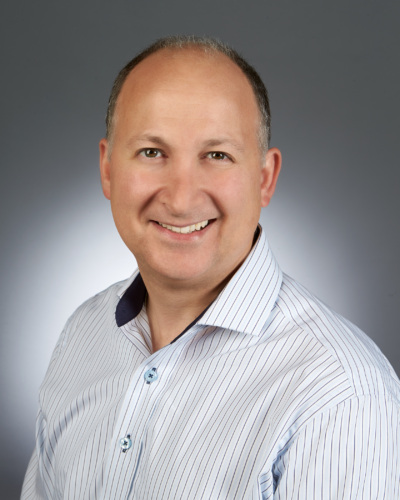 Headshot of a white man in a button up shirt with a grey background.