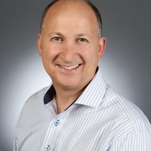 Headshot of a white man in a button up shirt with a grey background.