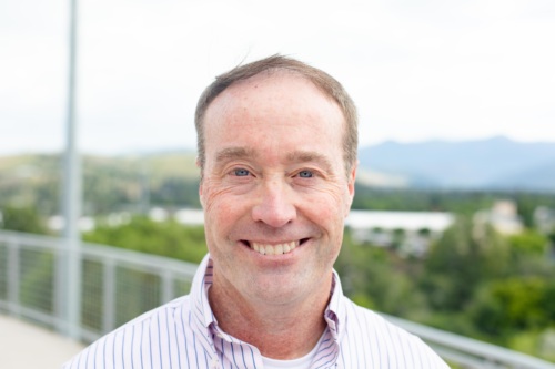 Headshot of Doug Seich, a white man wearing a collard shirt standing in front of scenic mountains