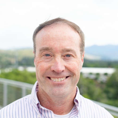 Headshot of Doug Seich, a white man wearing a collard shirt standing in front of scenic mountains