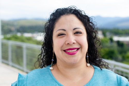 Headshot of Alice Garcia, a Latina woman with long curly black hair standing in front of scenic mountains