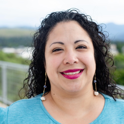 Headshot of Alice Garcia, a Latina woman with long curly black hair standing in front of scenic mountains