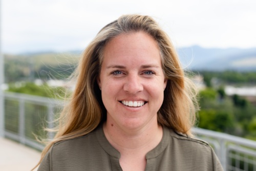 Headshot of Sara Hunold, a white woman with blonde hair standing in front of scenic mountains