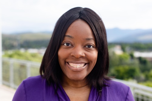 Headshot of a Black woman smiling in front of scenic mountains.