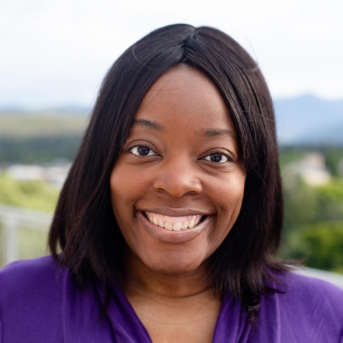 Headshot of a Black woman smiling in front of scenic mountains.