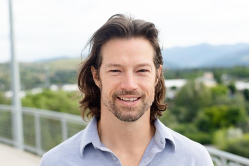 Headshot of Trip O'Connell, a white man with long brown hair in front of scenic mountains