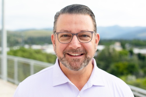 Headshot of Larry Danna, a white man with a salt and pepper beard in front of scenic mountains