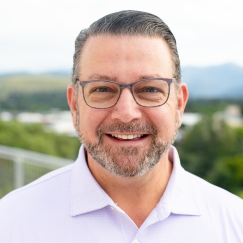 Headshot of Larry Danna, a white man with a salt and pepper beard in front of scenic mountains