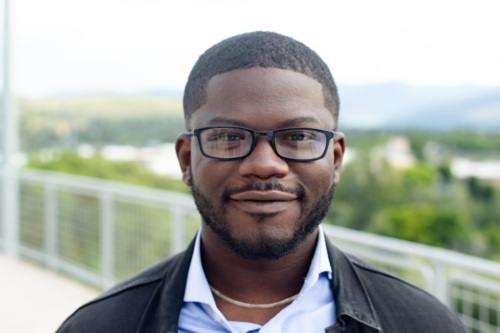 Headshot of a Dami Olaoye, a Black man wearing glasses in front of scenic mountains.