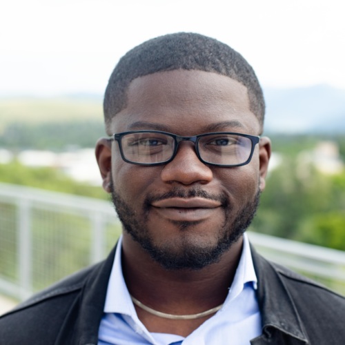 Headshot of a Dami Olaoye, a Black man wearing glasses in front of scenic mountains.