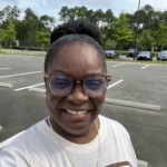 A selfie of Keisha Washington, a middle ages Black woman wearing a tshirt with trees in the background.