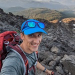 Selfie of Matt Demobowski, a white man wearing a hat and backpack hiking a mountain