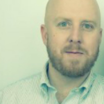 Headshot of Ryan Smither, a bald white man wearing a button up shirt with a white background.