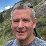 Headshot of Steve Woll, a white middle aged man wearing sunglasses atop his head with a mountain in the background.