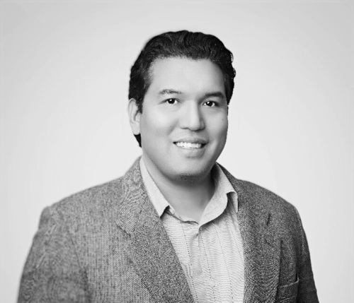 A black and white headshot of Ryan Enriquez, a middle aged latino man wearing a suit jacket.