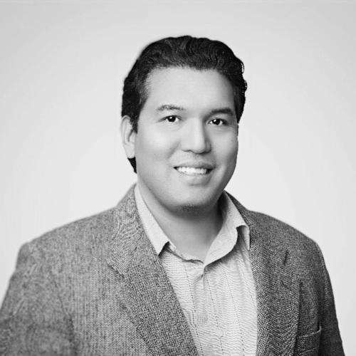 A black and white headshot of Ryan Enriquez, a middle aged latino man wearing a suit jacket.